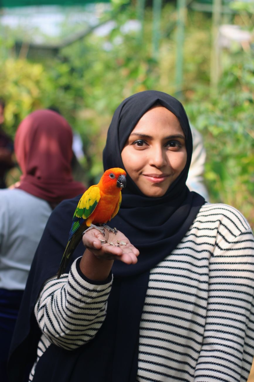 Young woman smiling with a Sun Conure perched on her hand